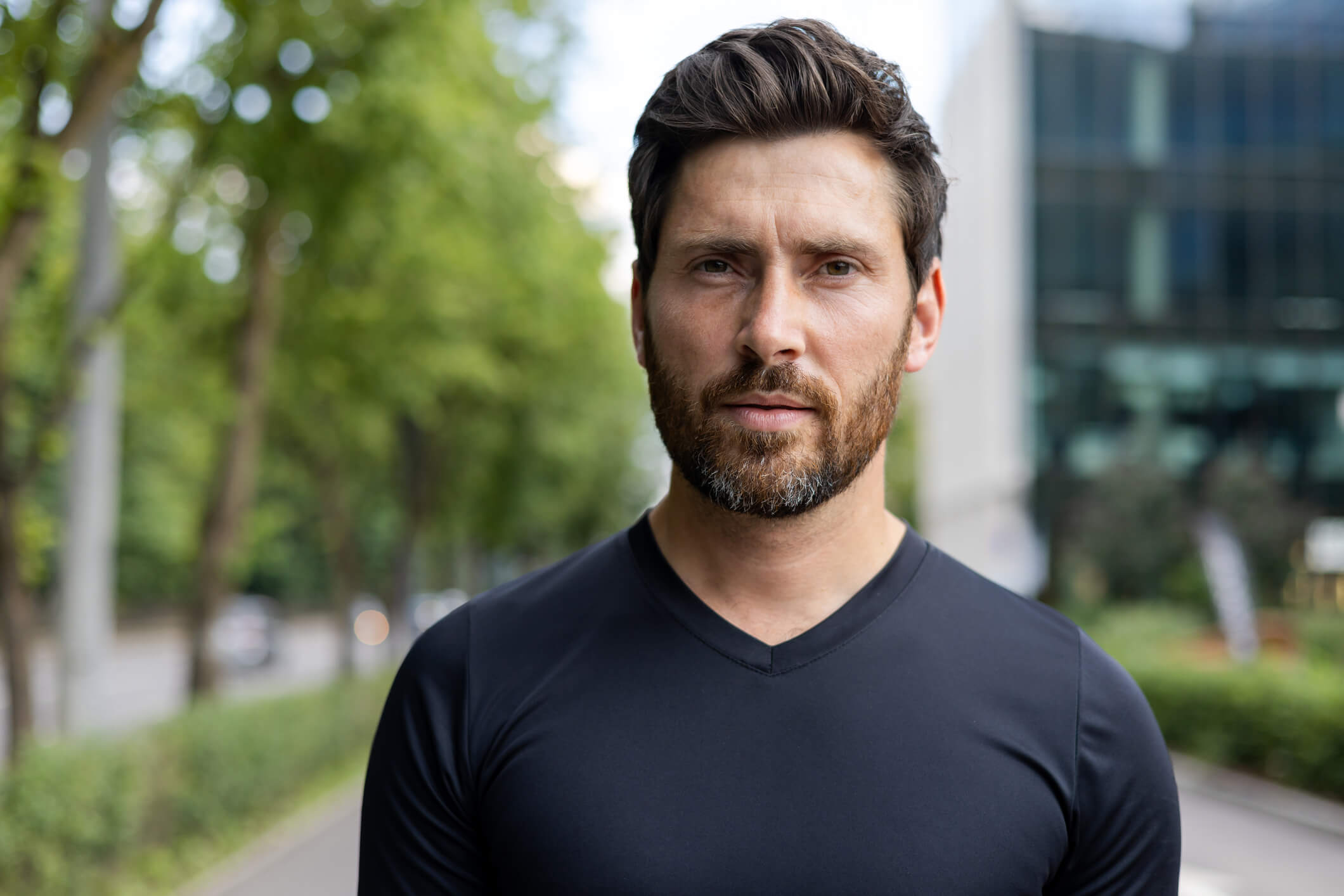Confident bearded man in casual attire standing outdoors with a focused expression
