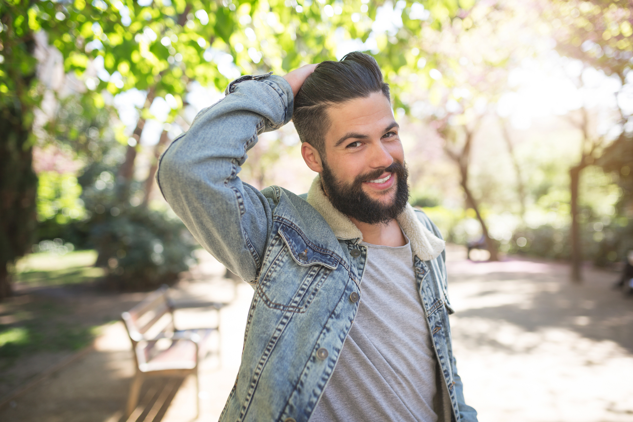 A photo of a handsome man standing on the alley in the park. He's posing to the photo and smiling happily.